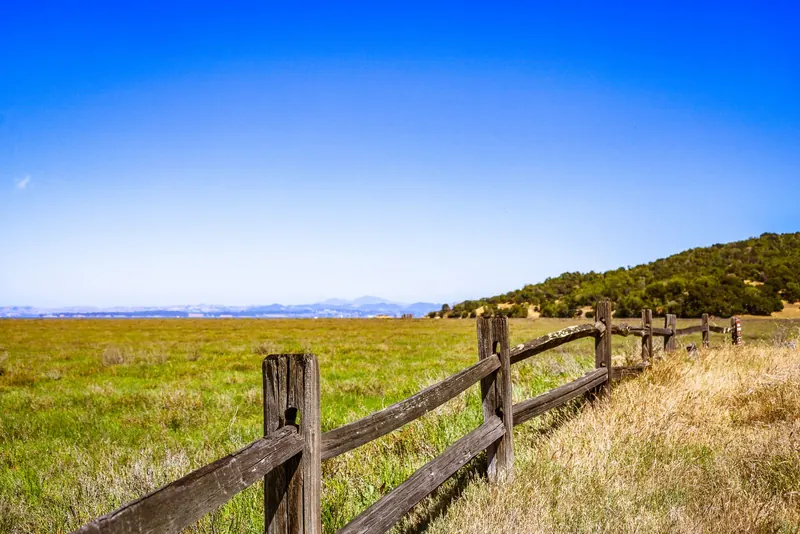 A weathered wooden rail fence running across open grassland toward wooded hills under a clear sky